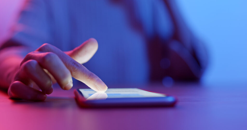 Primo piano di una mano che scorre su uno smartphone, illuminata da luci tendenti al viola