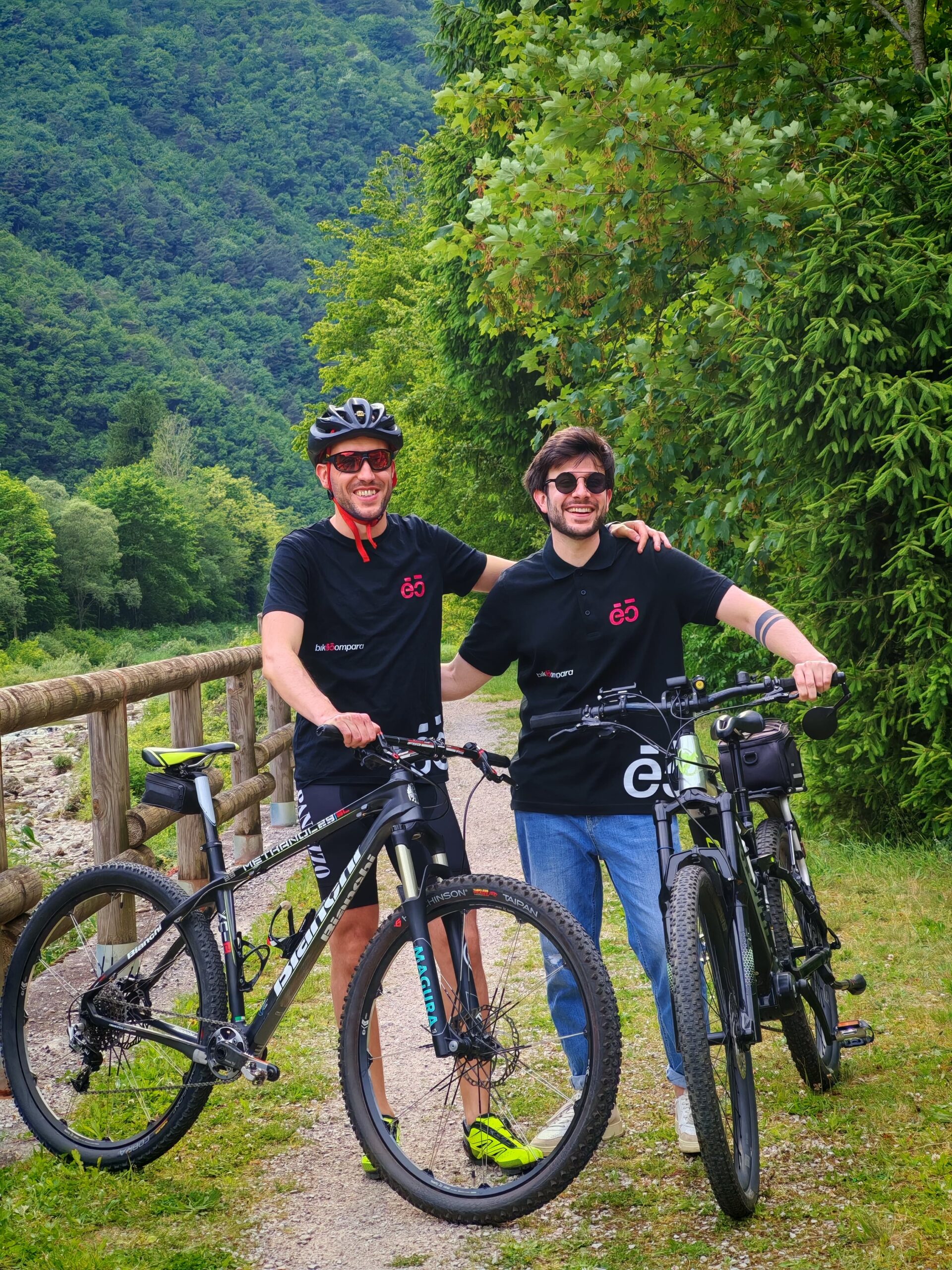 I due fondatori di Bikecompara sorridenti con maglia del brand e bici in ambiente naturale